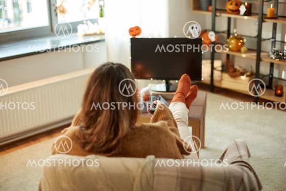 young woman watching tv at home on halloween