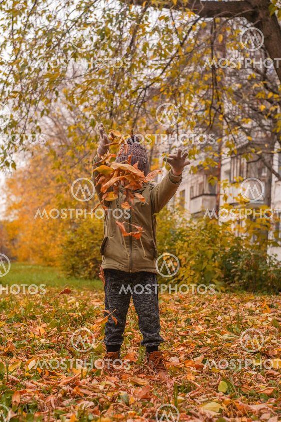 Little boy tossing leaves in autumn park.