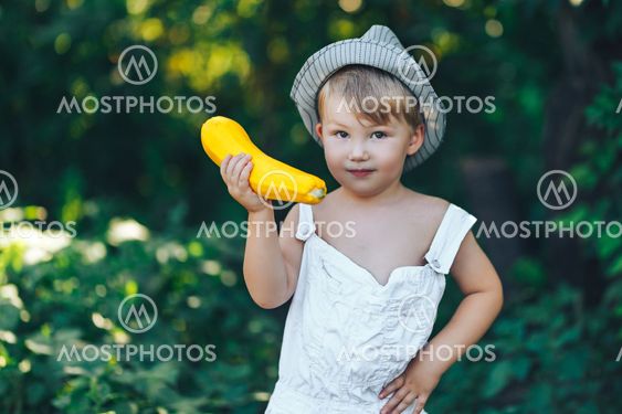 little boy holding yellow zucchini squash in summer...