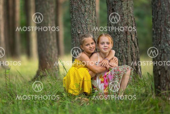 Little sisters are sitting near a tree in the Park.