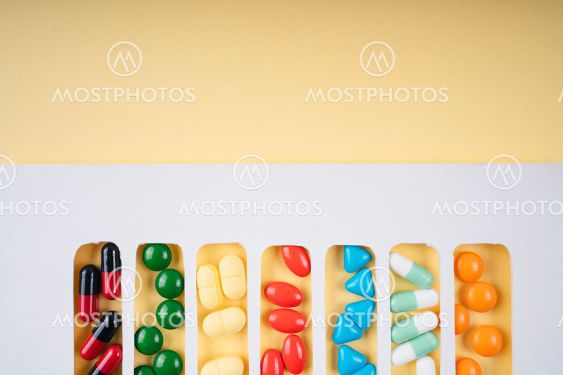 Colourful pills in white frame over yellow background.