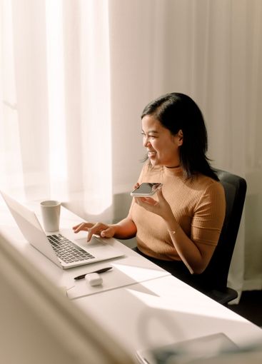 Happy businesswoman using laptop while talking through...