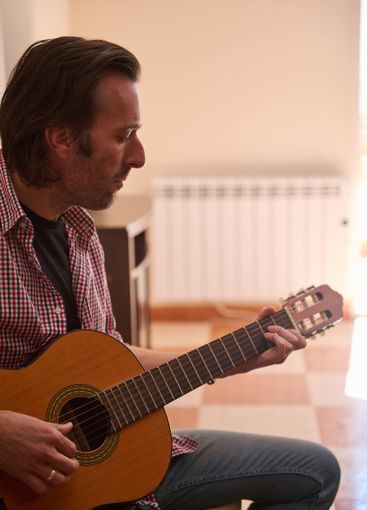 Man Playing Acoustic Guitar Indoors with Focus on...