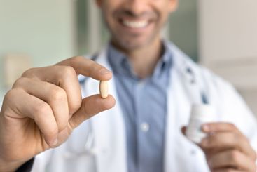 Hands of positive male doctor holding pill and bottle