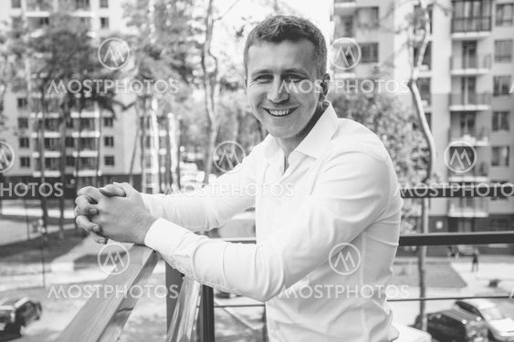 stylish smiling man in white shirt posing on balcony...