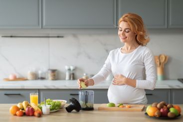 Pregnant woman preparing healthy smoothie with fresh...