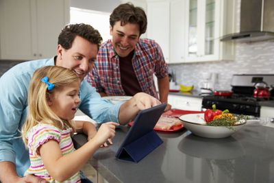 Girl using tablet in kitchen with male parents, close up