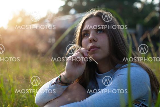 Teenage girl sitting in green grass in summer countryside.