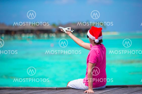 Young man in santa hat on white beach with miniature of...