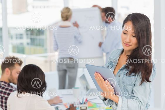 Asian woman using her tablet pc while her colleagues are working