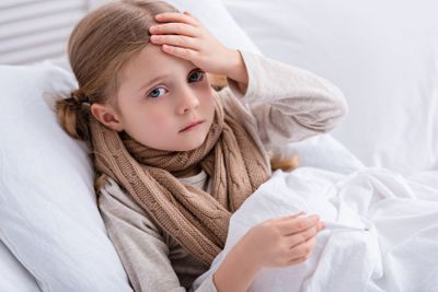 sick child with scarf over neck lying in bed, holding...