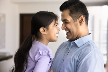 Cheerful loving Indian dad cuddling pretty daughter kid