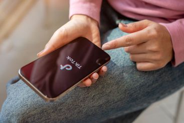 A close-up of a woman sits indoors, using TikTok...