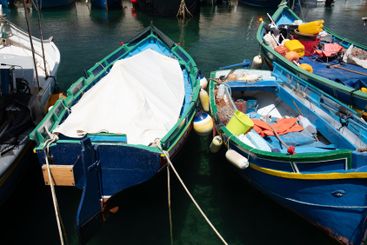 Colourful wooden fishing boats lie on the shore. Some of...