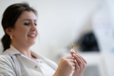 A focused nurse in a white lab coat carefully prepares a...