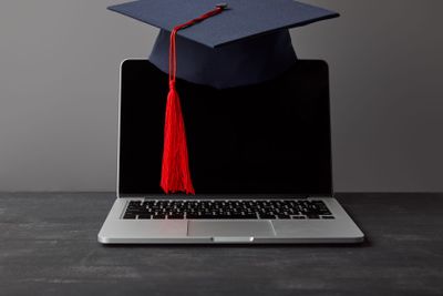 Laptop with blank screen and academic cap with red tassel...