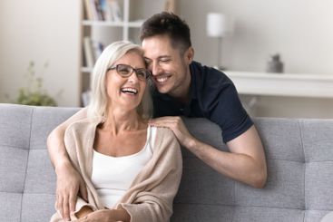 Affectionate adult son hug smiling aged mother sitting...