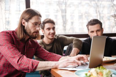 Happy men friends sitting in cafe while using laptop.
