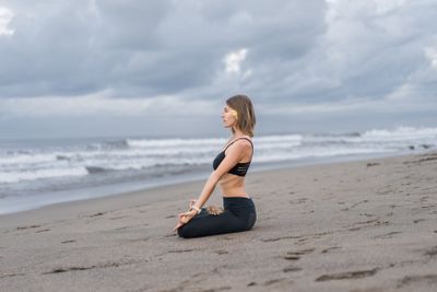 young woman practicing yoga in lotus pose on seashore