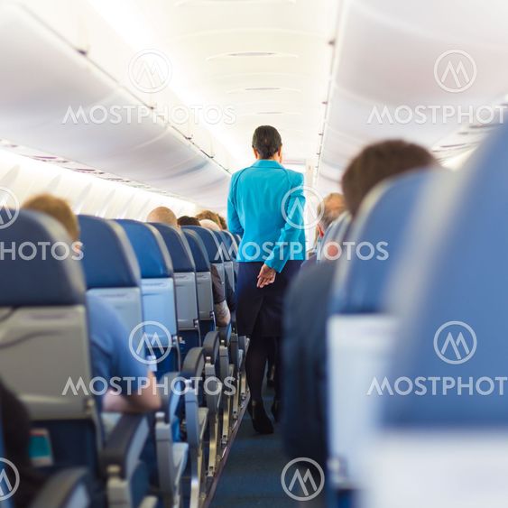 Interior of airplane with stewardess walking the aisle.