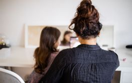 Mother and little daughter sitting at a desk and using a...