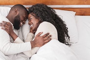 Black millennial couple cuddling in bed at home