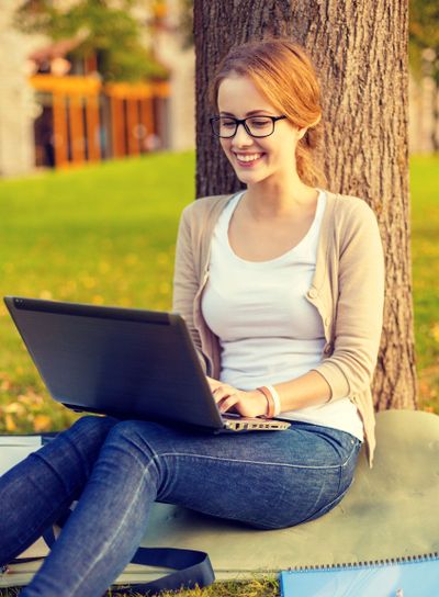 smiling teenager in eyeglasses with laptop