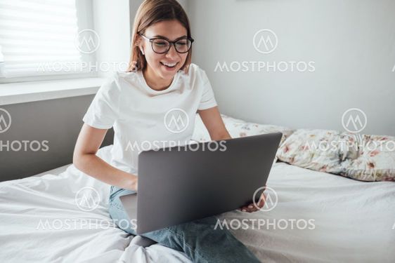 Young smiling woman uses laptop at home on the bed....