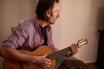 Man playing acoustic guitar while seated indoors during...