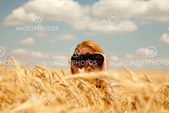 Redhead girl with binocular at wheat field.