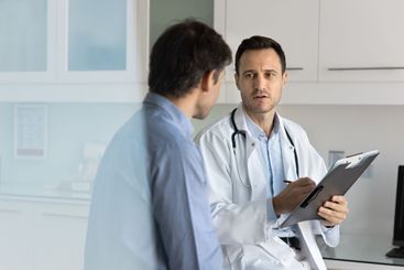 Serious doctor giving consultation to male patient,...
