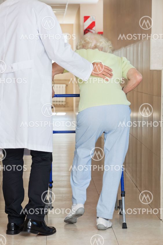 Doctor Assisting Senior Woman To Use Walker