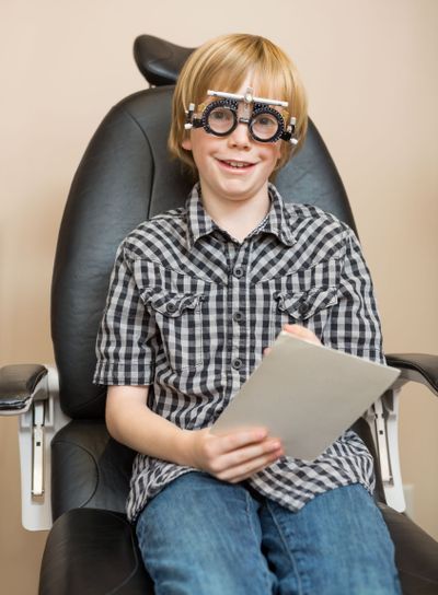 Boy With Trial Frame Holding Test Chart At Optician