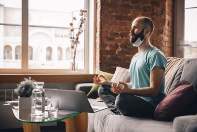 Young man doing yoga at home while being quarantine and...