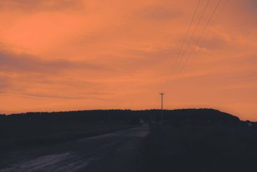 At dusk, the sky is a shade of orange and the power line...