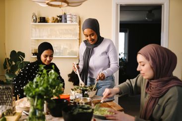 Smiling woman making salad while standing by friends...