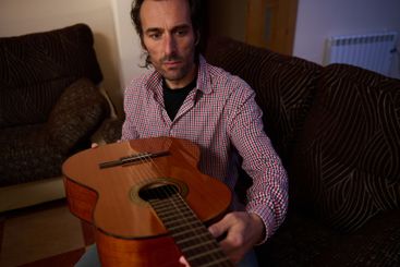 Man inspecting an acoustic guitar while sitting indoors...