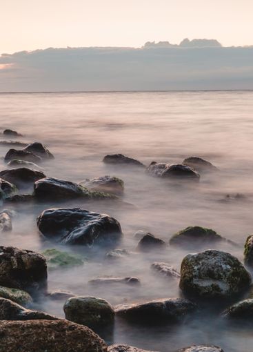 Calm seascape at twilight with smooth waves and rocky...