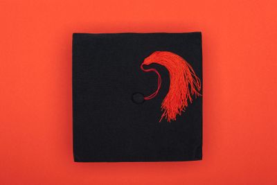 Top view of academic cap with tassel on red surface