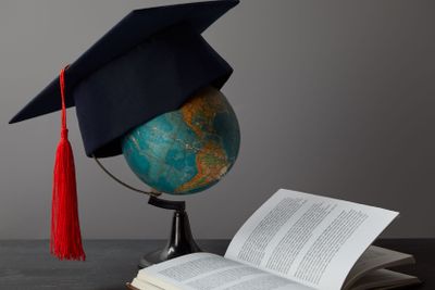 Globe, academic cap with red tassel and open book on...
