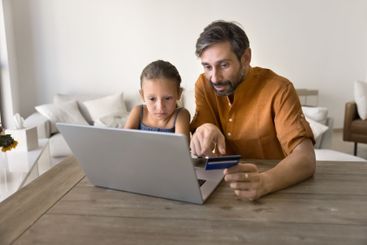 Man and little daughter buying goods using card and laptop