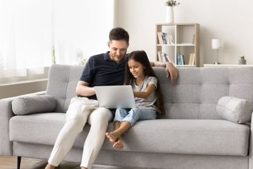Focused young father preteen girl sit on couch using laptop