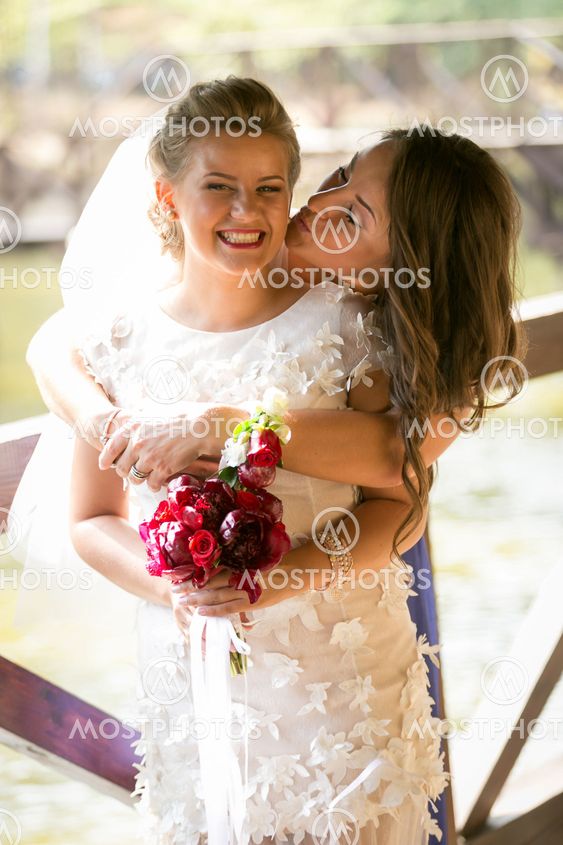 portrait of cute bridesmaid kissing laughing bride in cheek