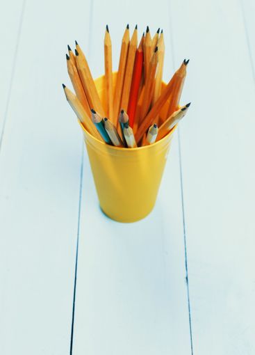 Assorted pencils in a yellow cup placed on a white...