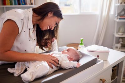 Happy mother changing the diaper of her baby at home on a...