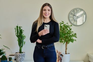 Confident young woman with smartphone in home interior