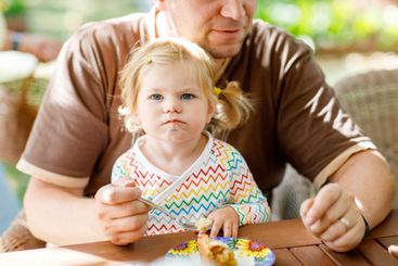 Young middle-aged father feeding cute little toddler...