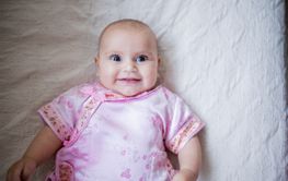 Happy baby girl in Asian pink attire lying down on a bed
