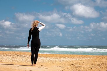 girl stands on the seashore in a black and white wetsuit...