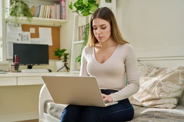 Young woman working at home, sitting on couch using laptop